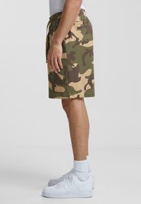 Camo print shorts in olive green, light brown, and dark brown. Crafted from cotton with an elastic waistband and side pockets.