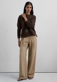 Sudadera marrón de manga larga con aberturas en los laterales, combinada con pantalones de pierna ancha de tiro alto en color beige y sandalias negras con tiras.
