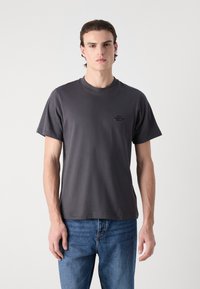Mørk grå bomulls t-skjorte med korte ermer, rund hals, og en liten trykt logo på venstre bryst. Kombinert med blå jeans.