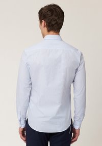 Camisa de hombre de manga larga, azul claro con rayas blancas verticales. Cuello clásico, puños abotonados y dobladillo redondeado. Textura de algodón suave.