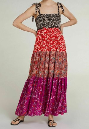 Donna che indossa un abito lungo senza maniche con la parte superiore a stampa leopardata, gonna a toppe rosse e floreali, spalline annodate e sandali neri.