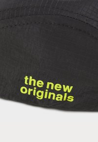 Fekete textília rácsos mintával, rajta a "the new originals" felirat élénk sárgában. Simogató tapintású, nem található rajta látható fémalkatrész vagy díszítés.
