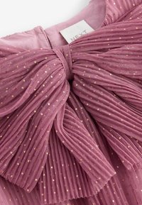 Robe violette claire à volants avec des taches dorées, dotée d'un grand nœud au niveau de l'encolure et d'un tissu texturé plissé.