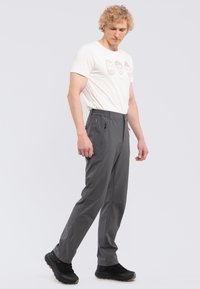 Graue, leichte Hose im Slim-Fit-Stil mit seitlichen Reißverschlusstaschen, elastischem Bund und verstärkten Nähten. Kombiniert mit einem weißen T-Shirt mit grafischem Aufdruck.