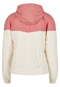 Kurtka z kapturem z różową górną częścią i kremowym dolnym fragmentem. Wykonana z lekkiego, gładkiego materiału z elastycznymi mankietami i dolnym wykończeniem.