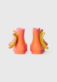 Bottes de pluie en caoutchouc orange avec des tiges roses, ornées d'accents de papillons colorés à l'arrière. Texture lisse et forme arrondie.
