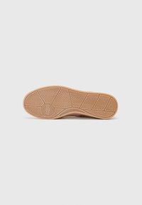 Semelle de chaussure en caoutchouc brun avec un motif en zigzag texturé, présentant un logo circulaire au centre. Profil plat avec une légère courbe.