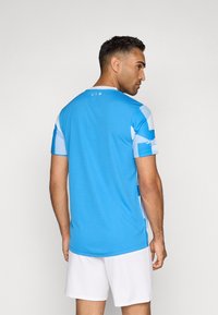 Svijetloplava atletska majica s kratkim rukavima, s okruglim izrezom i bijelim bočnim panelima s geometrijskim uzorcima.