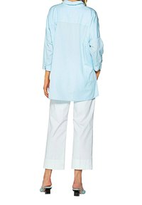 Light blue long-sleeve shirt with a loose fit, button detailing at the cuffs, worn with white wide-leg pants and blue heeled sandals.
