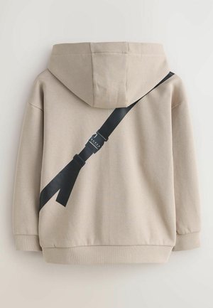 Beiger Hoodie mit Kapuze, der am Rücken ein schwarzes diagonales Riemendesign mit Schnallendetail aufweist. Strukturierter Stoff.