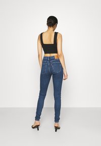 Top negro corto con tirantes anchos combinado con jeans ajustados de mezclilla azul. Los jeans presentan una etiqueta beige, bolsillos traseros y una silueta ajustada.