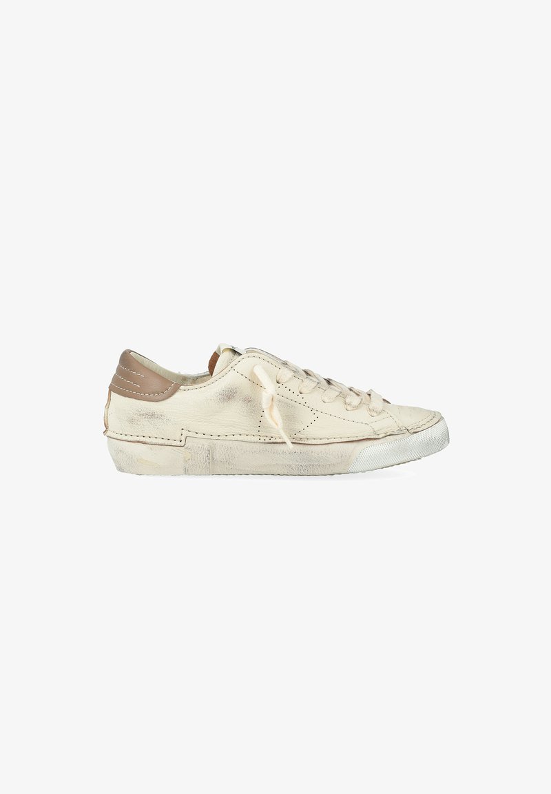 Baskets basses en cuir blanc usées avec un patch beige au talon, présentant des éraflures visibles, des plis et des lacets noués sur un fond blanc.