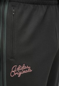 Μαύροι polyester joggers με πράσινες πλαϊνές ρίγες, που διαθέτουν τσέπη με φερμουάρ και ροζ κεντημένο λογότυπο "Adidas Originals".