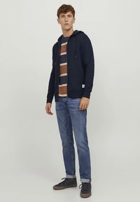 Laivastonsininen vetoketjullinen huppari, puuvillasekoitetta, jossa kiristysnauhallinen huppu. Yhdistetty raidalliseen pyöreäkaulaiseen paitaan, vaaleansinisiin farkkuihin ja tummiin lenkkareihin.