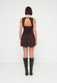 Καφέ μίνι φόρεμα με εφαρμοστό μπούστο και φουσκωτή φούσ τα, με άνοιγμα στην πλάτη σε σχήμα κλειδαρότρυπας και υφασμάτινη επένδυση, συνδυασμένο με μαύρες μπότες μέχρι το γόνατο.