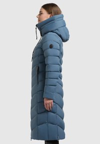 Garšs zils pūkains mētelis ar vertikālu un dimanta formas quiltēšanu, augstu apkakli un rāvējslēdzēja kabatām. Mācies ar regulējamiem aukliņām.