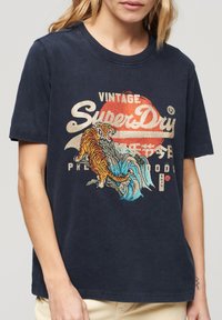T-shirt en coton bleu marine avec un graphique vibrant de tigre et de vague, avec la marque "SuperDry" en couleurs claires et un col rond.