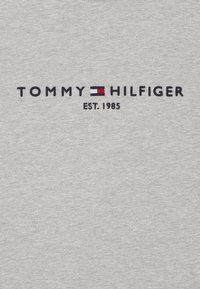 Šedé bavlněné tričko s vyšitým textem "TOMMY HILFIGER EST. 1985" v černé barvě a červeným a bílým akcentem mezi nimi.