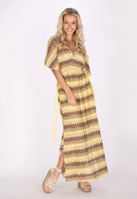 Abito lungo con motivo a zigzag in marrone, giallo e bianco. Presenta maniche corte, scollatura a V e uno spacco laterale. Abbinato a sandali con zeppa.