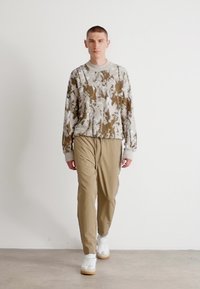 Brun och beige mönstrad sweatshirt med rund hals, i kombination med tanfärgade smalare byxor och vita sneakers med beige detaljer.