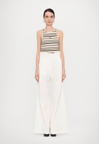 Top a righe beige abbinato a pantaloni bianchi a gamba larga. L'outfit presenta una silhouette aderente e dettagli plissettati.
