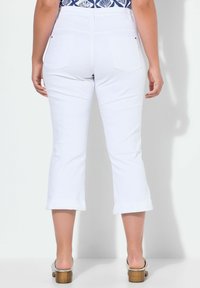 Pantalones blancos ajustados con cintura ceñida y dobladillo amplio. Presenta dos bolsillos traseros y una textura suave, combinados con sandalias de tacón plateadas.