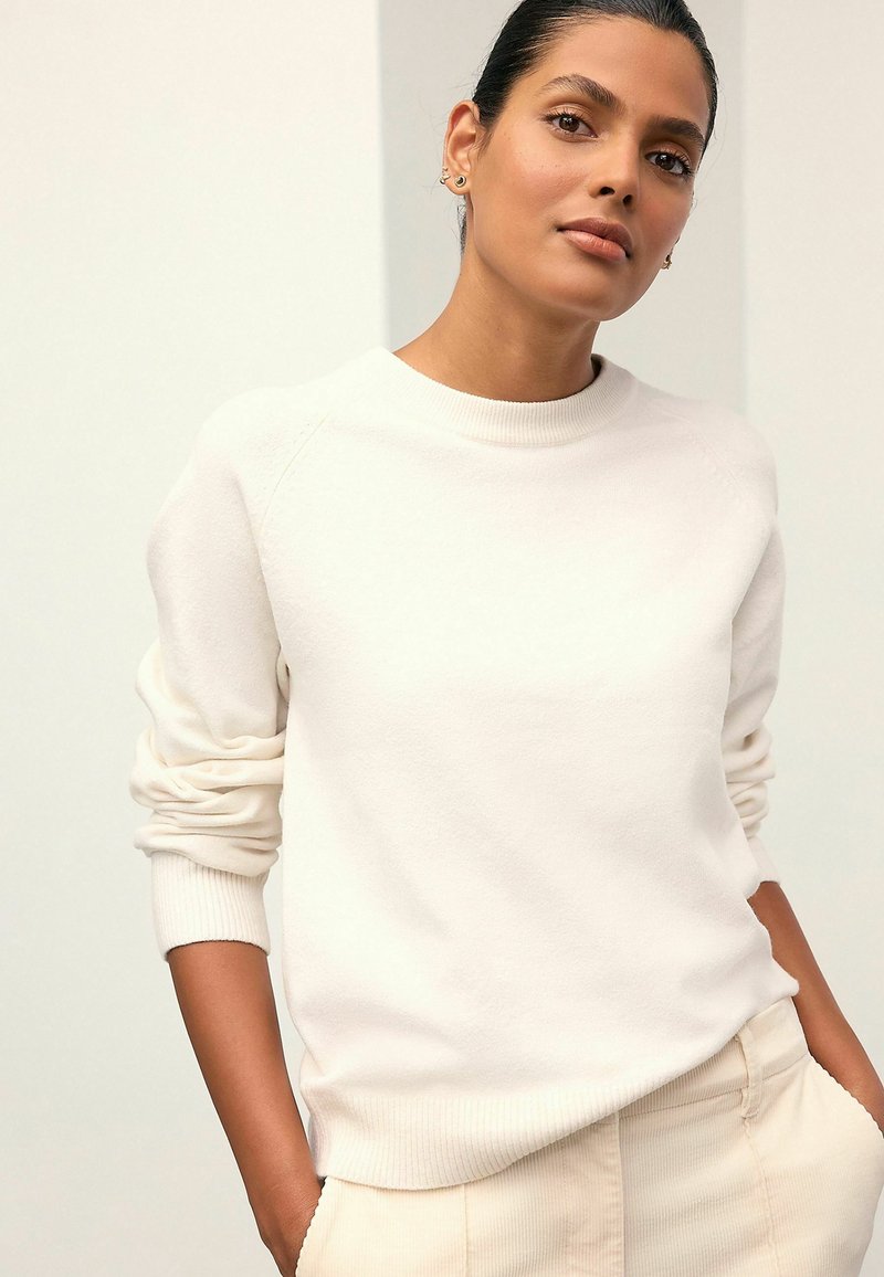Hanorac alb cu guler rotund, dotat cu manșete și tiv din tricot. Textură moale, croială lejeră, asortat cu pantaloni de culoare deschisă. Design minimalist.