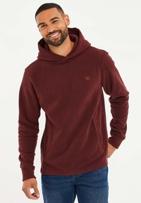 Bordeauxroter Fleece-Hoodie mit einer Fronttasche, weichem Material, verstellbarem Kordelzug in der Kapuze und dezentem Logodetail auf der Brust.