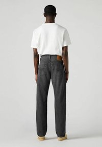 Jeans neri a gamba dritta con una patta in pelle sulla vita posteriore, abbinati a una maglietta bianca. Tessuto liscio, vestibilità casual.