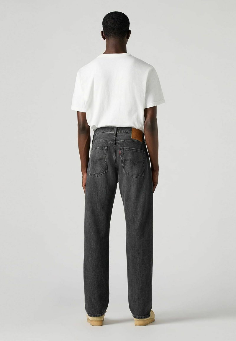 Jeans negros de pierna recta con un parche de cuero en la parte trasera de la cinturilla, combinados con una camiseta blanca. Textura de tela suave, ajuste casual.