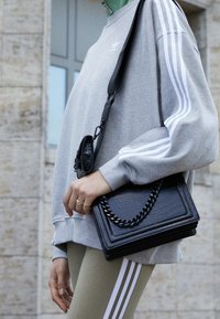 Svart texturerad handväska med kedjedetaljer, bärs tillsammans med en grå sweatshirt med vita ränder och olivgröna leggings.