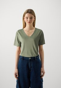 T-shirt vert à manches courtes et col en V en tissu doux, associé à un pantalon en denim sombre à taille haute et coupe ample avec poches latérales.