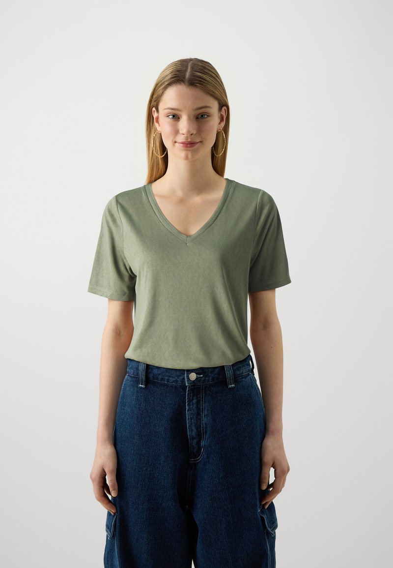 T-shirt vert à manches courtes et col en V en tissu doux, associé à un pantalon en denim sombre à taille haute et coupe ample avec poches latérales.