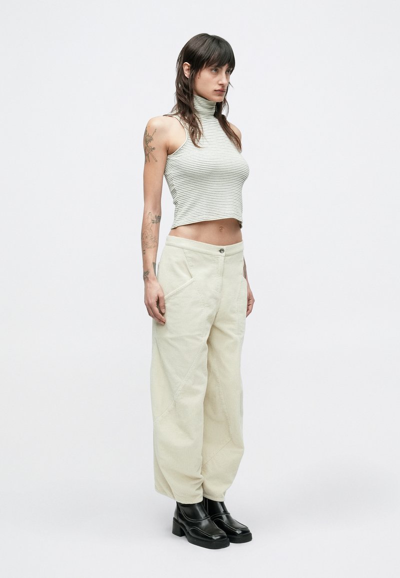 Graues gestreiftes ärmelloses Oberteil mit Stehkragen, kombiniert mit cremefarbenen weiten Cordhosen und schwarzen Plateaustiefeln. Glatte Textur, lockere Passform.