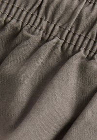 Tissu marron avec un tissage texturé, présentant des coutures froncées et une apparence douce et drapée. Accent sur les détails et la profondeur du tissu.