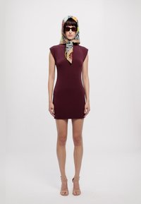 Βουργουνδίζα εφαρμοστή φόρμα με κοντά μανίκια, λεία υφή. Το μοντέλο φορά ένα πουκάμισο με σχέδιο και σκούρα γυαλιά ηλίου, στέκεται σε ουδέτερο φόντο.