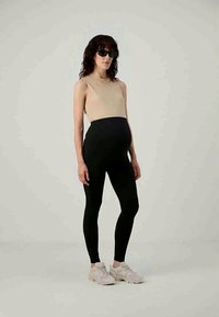 Bežinė striukė be rankovių, derinama su juodomis kelnėmis aukštu liemeniu. Modelis dėvi baltus sportinius batelius ir tamsius akinius nuo saulės. Paprastas, prigludęs dizainas.