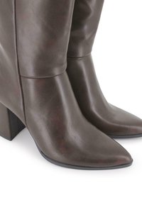 Botas de cuero marrón oscuro con punta afilada y tacones de bloque de altura media, textura suave y detalles de costura mínimos sobre un fondo blanco.