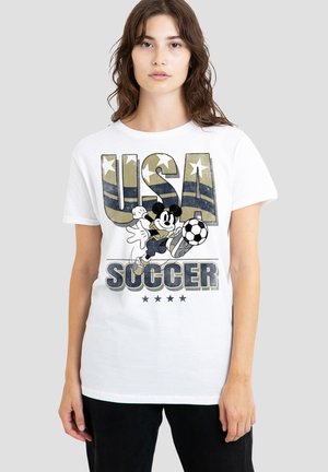 Young woman wearing a white T-shirt with "USA" in camo print, Mickey Mouse kicking a soccer ball, and the word "SOCCER" below.