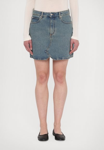 Denim mini nederdel med en asymmetrisk søm fortil, lys blå vask, fem-lomme design og synlig metalhardware. Funktionel frontknap.