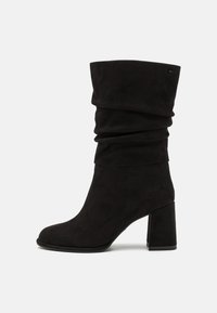 Bottine en daim noir à design décontracté, bout rond et talon épais. La bottine présente une texture lisse et des accents minimalistes.