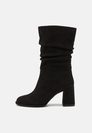 Bottine en daim noir à design décontracté, bout rond et talon épais. La bottine présente une texture lisse et des accents minimalistes.