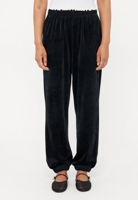 Svarte velour sweatpants med elastisk midje, smale mansjetter og en glatt tekstur. Brukt sammen med enkle sorte sko.