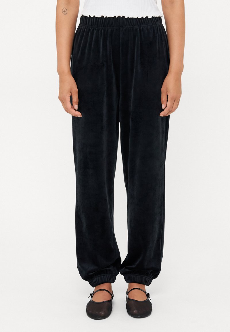 Svarte velour sweatpants med elastisk midje, smale mansjetter og en glatt tekstur. Brukt sammen med enkle sorte sko.