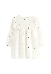 Weißes Kleinkinderkleid mit langen Ärmeln, das einen gerafften Ausschnitt und verstreute rote und pinkfarbene Herzen auf dem Stoff hat.