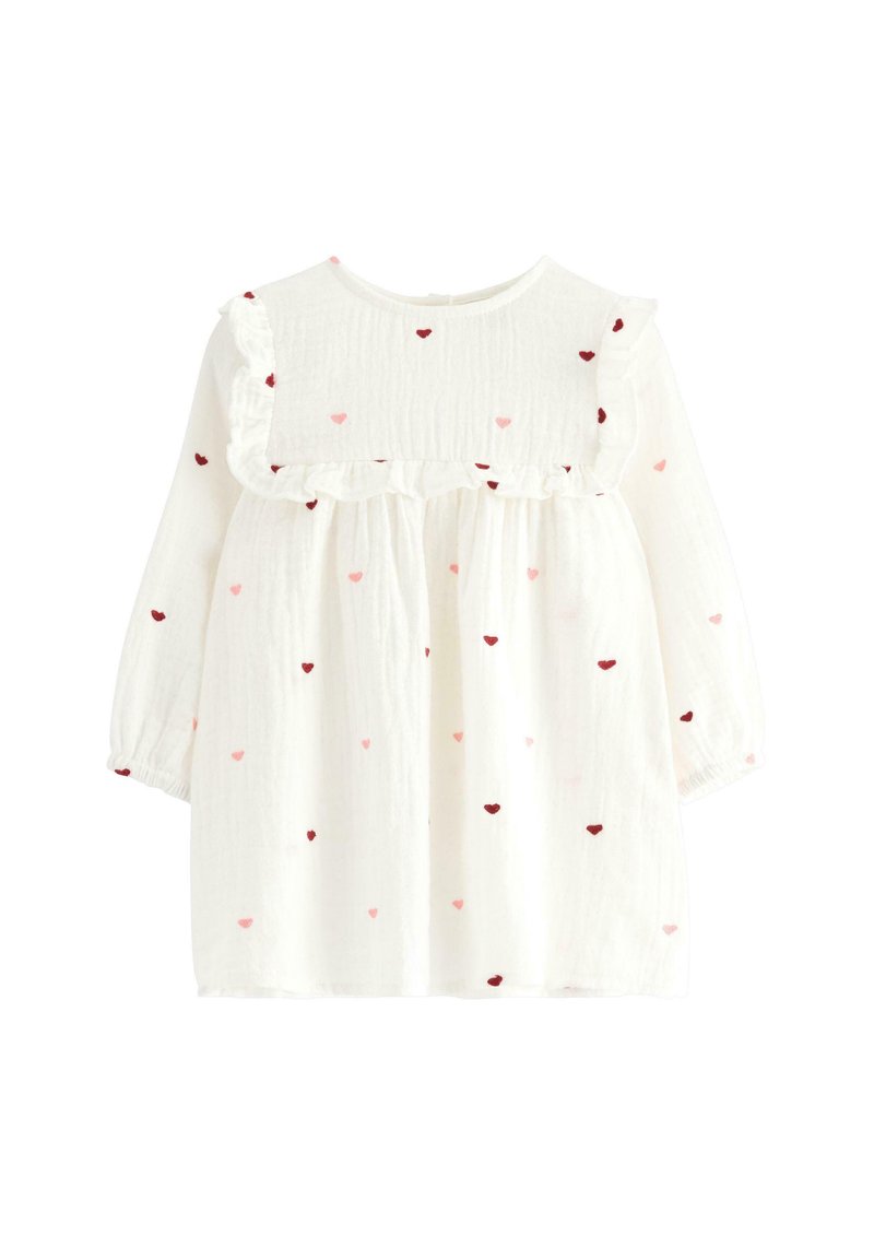 Weißes Kleinkinderkleid mit langen Ärmeln, das einen gerafften Ausschnitt und verstreute rote und pinkfarbene Herzen auf dem Stoff hat.