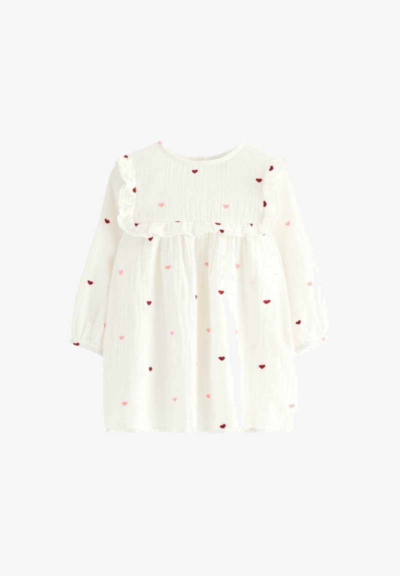 Robe blanche pour enfant avec des manches longues, dotée d'un col à volants et de motifs de cœurs rouges et roses éparpillés sur le tissu.