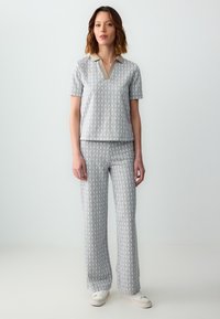 Grijze set met korte mouwen en broek, met een herhalend licht patroon, voorzien van een V-hals en een contrasterende kraag. Zachte stoffen textuur.