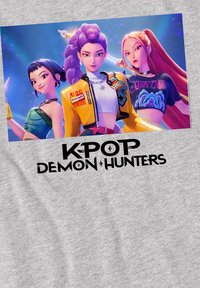 Gray fabric t-shirt featuring a colorful printed design of three animated characters and the text "K-POP DEMON HUNTERS" in bold black lettering.