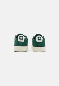 Green suede sneakers with white rubber soles. Includes a round logo with a star on the heel and 'CONVERSE' text above it.
